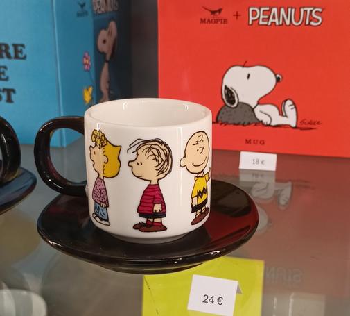 Eine mokkatasse in einer Vitrine abgebildet sind von links nach rechts Sally, Linus, und Charlie aus dem Peanuts Universum