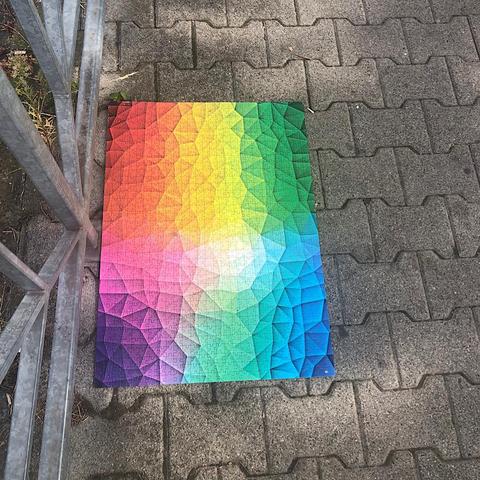 foto: auf sonnenbeflecktem gehwegpflaster liegt ein abstraktes poster in spektralfarben. es entpuppt sich als zusammengeklebtes puzzle.