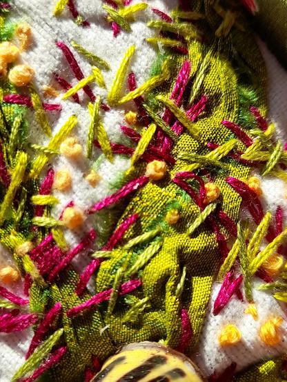 Detail of the wild stitches on white background fabric and yellowish green silk ribbon. The stitches are placed like strokes of a paintbrush.