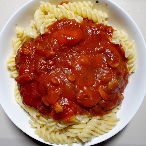 Nudeln, Tomatensoße und ein paar Champignons auf weißem Teller.