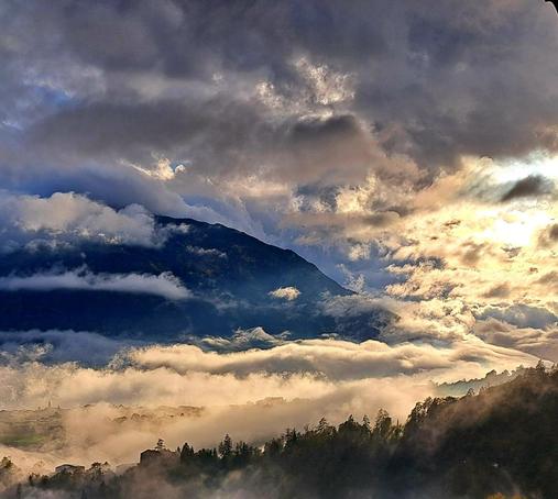 Dichte Wolken im Tal mit Sonne und dunklen Berghängen.