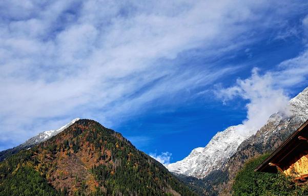 Berge, teils schneebedeckt, unter blauem Himmel mit Wölkchen.