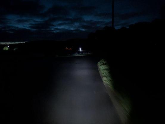 Dunkler Radweg am frühen Morgen mit einem hellen Lichtpunkt (= entgegenkommender Radfahrer) in der Ferne
