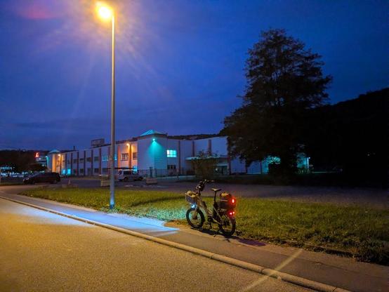 Mein Fahrrad mit eingeschaltetem Rücklicht steht frühs an einem beleuchteten Straßenrand vor der Firma