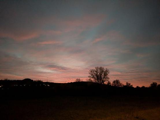 Dämmerungshimmel mit vereinzelten Wolken über einer dunklen Landschaft mit Baum- und Hügel-Silhouetten