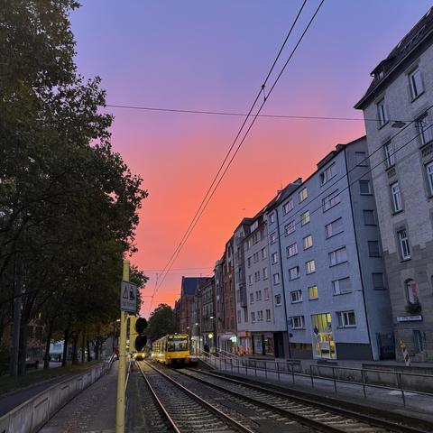 Stadtbahnhaltestelle mit einer gelben Stadtbahn unter rot leuchtendem Sonnenaufgang