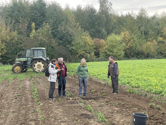 Jan vom Kölner Ernährungsrat auf dem Acker im Gespräch mit einer Bäuerin und 2 Bauern.