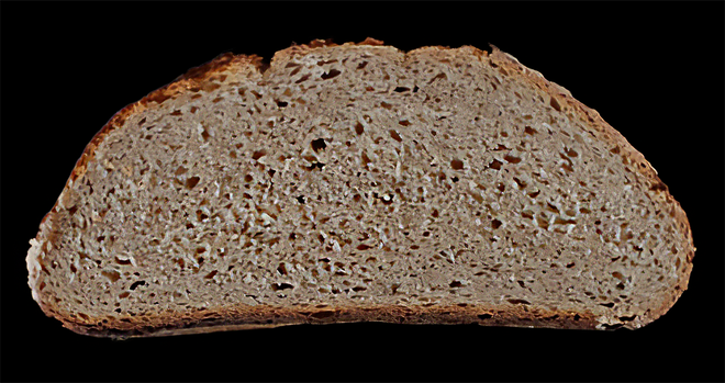 Aufsicht auf eine frische halbrunde Scheibe Brot, die aussieht wie das im Tröt geschilderte, freigestellt auf schwarzem Hintergrund.