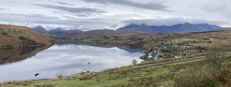 Photo shows a view up Loch Harport with Carbost to the right and the hills of Skye in the background.