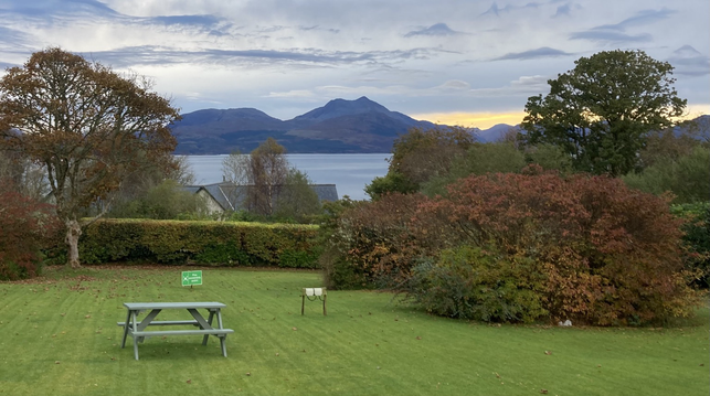 The manicured lawns of Duisdale House in the foreground with a small patch of sea and some hills in the background under a grey leaden sky