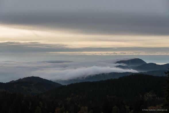 Wetterwechsel im Schwarzwald, aufgenommen als Zeitraffer vom Herzogenhorn. Rechts im Bild ist der Belchen zu sehen. Der Himmel ist zunächst milchig weiß und bezieht sich zunehmend mit Wolken. In den Tälern liegt Nebel, der im Zeitraffer sichtbar über die Bergrücken zieht. Der Belchen wird zeitweise von Wolken umgeben, danach ist der Gipfel wieder frei. / Weather change in the Black Forest, recorded as a timelapse from Herzogenhorn. The Belchen is visible on the right. The sky is initially milky white and gradually becomes overcast. Fog lies in the valleys and, as visible in the timelapse, slowly moves across the mountain ridges. The Belchen is occasionally surrounded by clouds; afterwards, the summit is clear again.